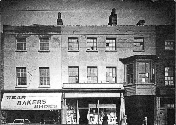 view of two 3 storey shops, followed by an archway (built over) and a glimpse of a third 3 storey shop