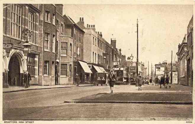 Quiet street scene with a lady in a fur-trimmed knee-length coat approaching, two trams, a van and motor car in the background