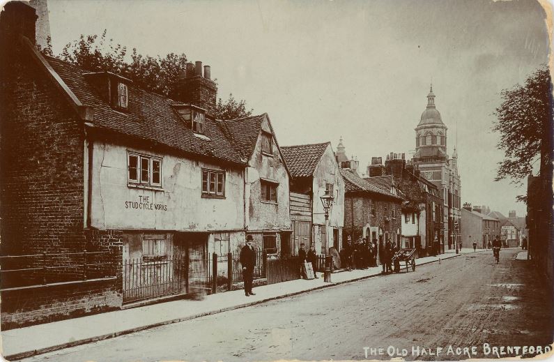 Sepia view of road with assortment of old buildings on the left side, no traffic