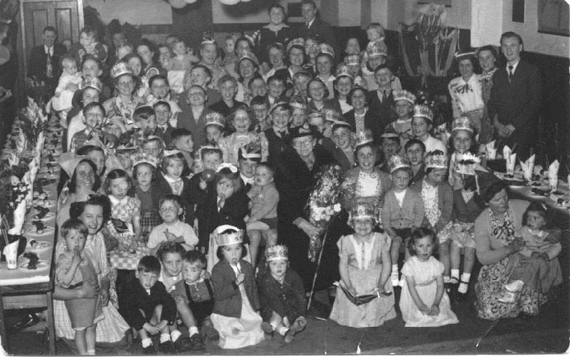 Hall packed with over 80 people, many children, with tables down either side