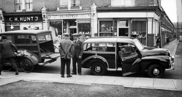 B/W photo showing a butchers and grocers shop with cars and people