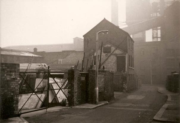 Narrow road, yard on left, looking towards High Street, gas works ahead