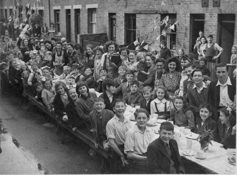 Over 40 happy children sitting at long table with adults standing behind