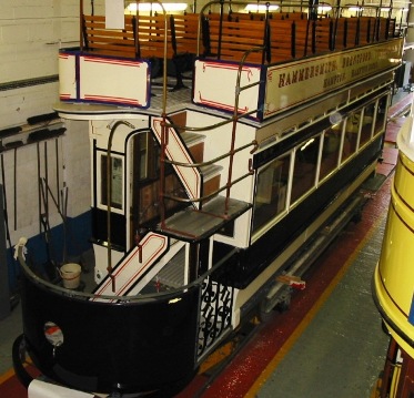 Open top tram with cream, black and red paintwork, wooden slat seats